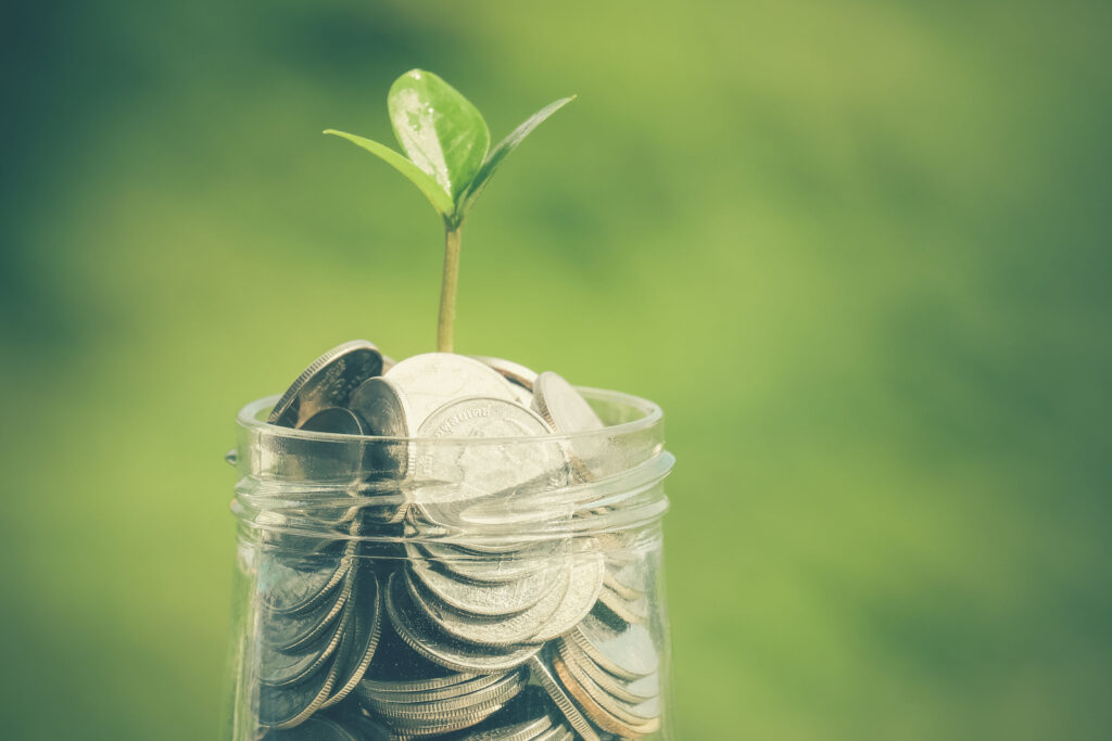 Glass jar filled with coins and a small green plant sprouting on top, symbolizing financial growth and savings